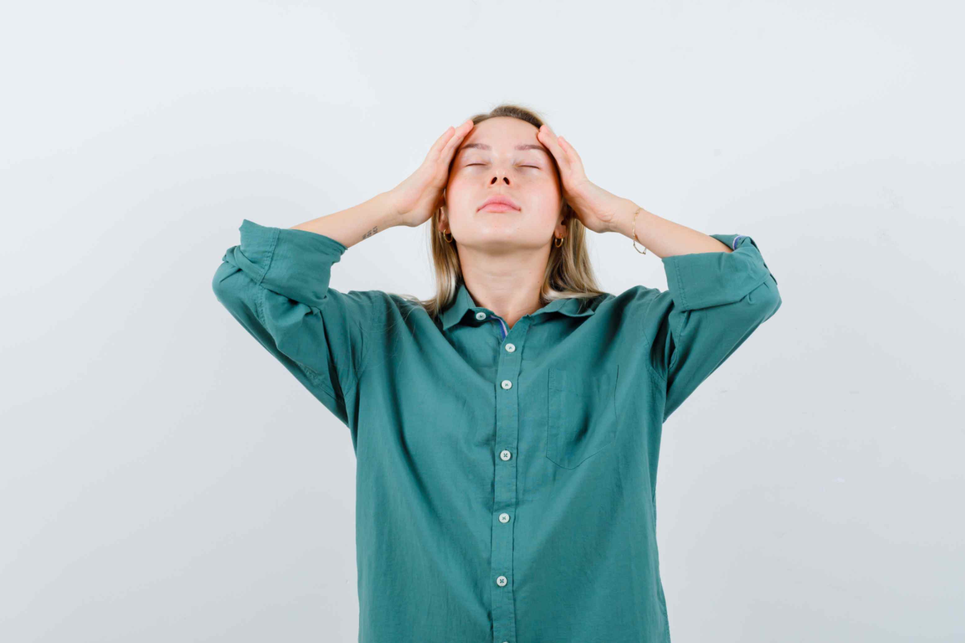 Woman in a green shirt holding her head with closed eyes, appearing stressed or overwhelmed.